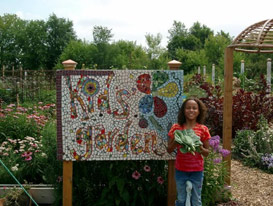 A girl in front of the Kids' Garden sign.